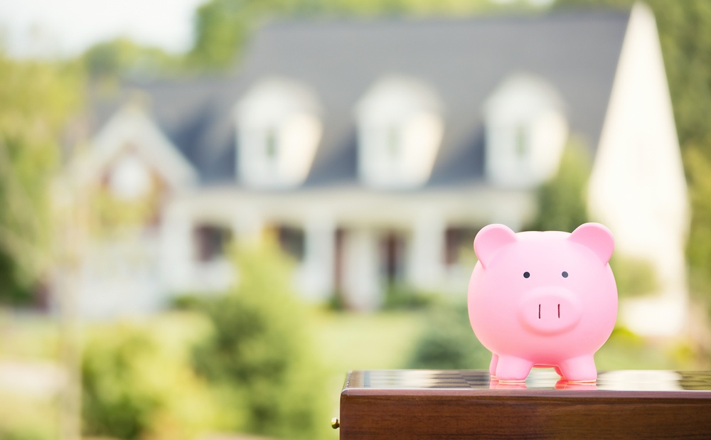 Real estate sale, home savings, loans market concept. Housing industry mortgage plan and residential tax saving strategy. Piggy bank isolated outside home on background. Focus on piggybank. Homeowner 